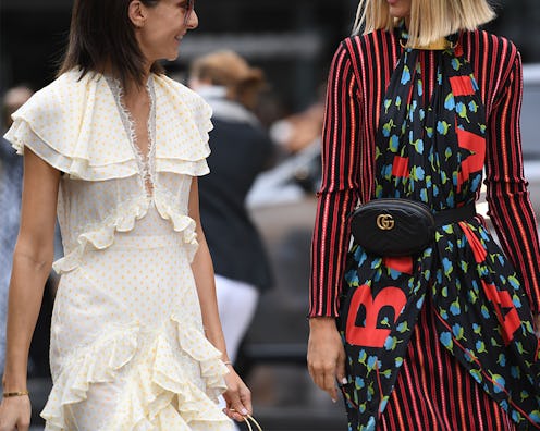 Two women walking down the street, one in a long white ruffled dress and the other in a stripy dress...