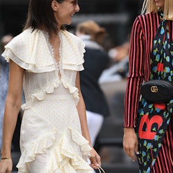 Two women walking down the street, one in a long white ruffled dress and the other in a stripy dress...