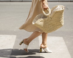 A woman walking in a beige linen dress, white-beige mules and a large jute bag