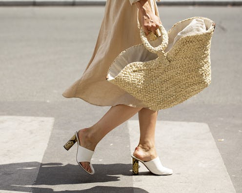 A woman walking in a beige linen dress, white-beige mules and a large jute bag