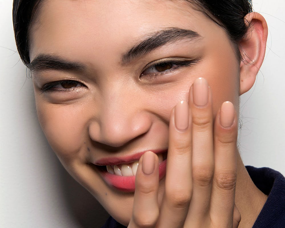 A brunette short-haired woman who uses the best exfoliating serums, smiling with her and over her fa...