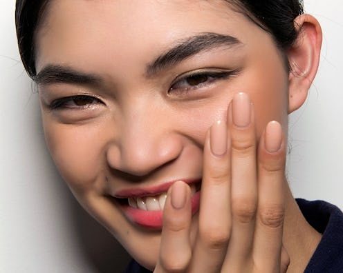 A brunette short-haired woman who uses the best exfoliating serums, smiling with her and over her fa...