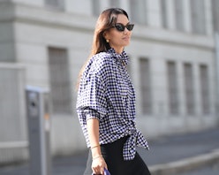 A woman in a blue and white gingham button-up shirt and a black dress crossing the street