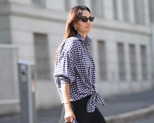 A woman in a blue and white gingham button-up shirt and a black dress crossing the street