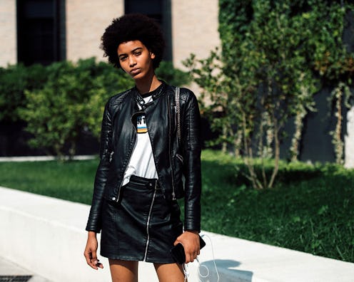 A curly woman wearing a black leather jacket and a matching skirt with a graphic tee