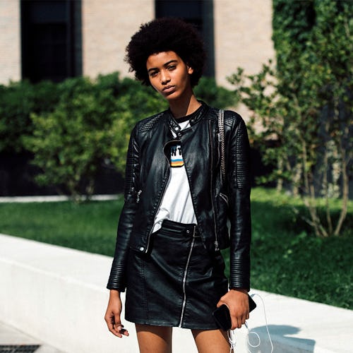 A curly woman wearing a black leather jacket and a matching skirt with a graphic tee