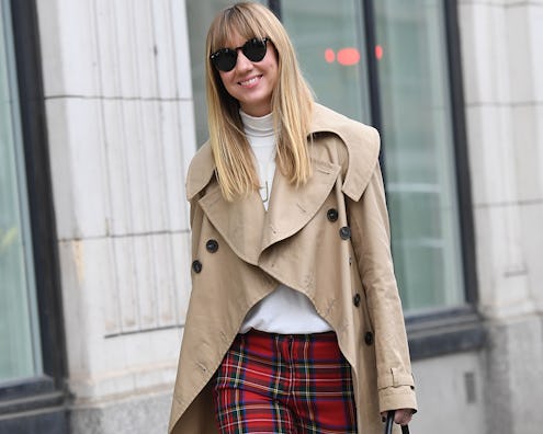 A woman walking in a light brown coat and in red plaid fall pants