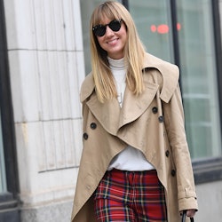 A woman walking in a light brown coat and in red plaid fall pants