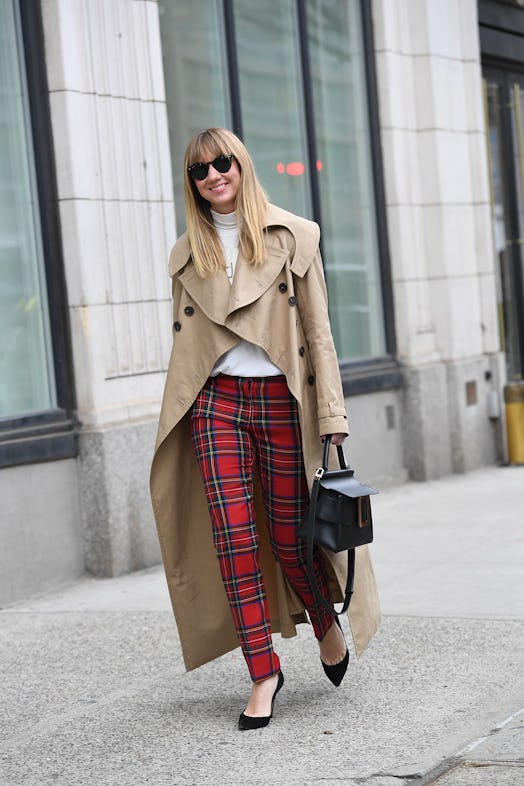 A woman walking while wearing a light brown coat and in red plaid fall pants