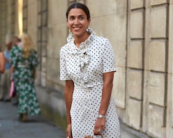 A black-haired woman posing in a white dress with black dots