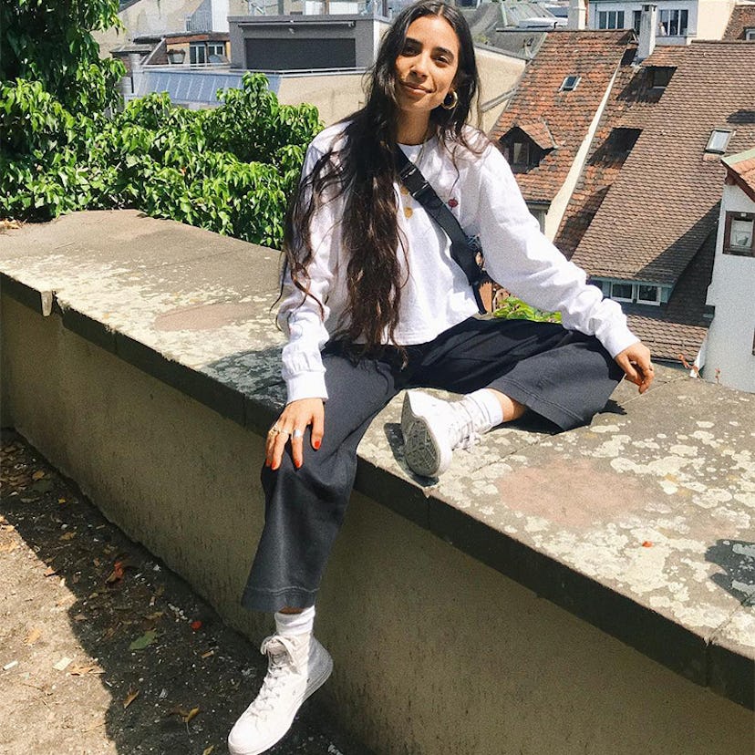 A black-haired girl posing while wearing white leather high-top sneakers